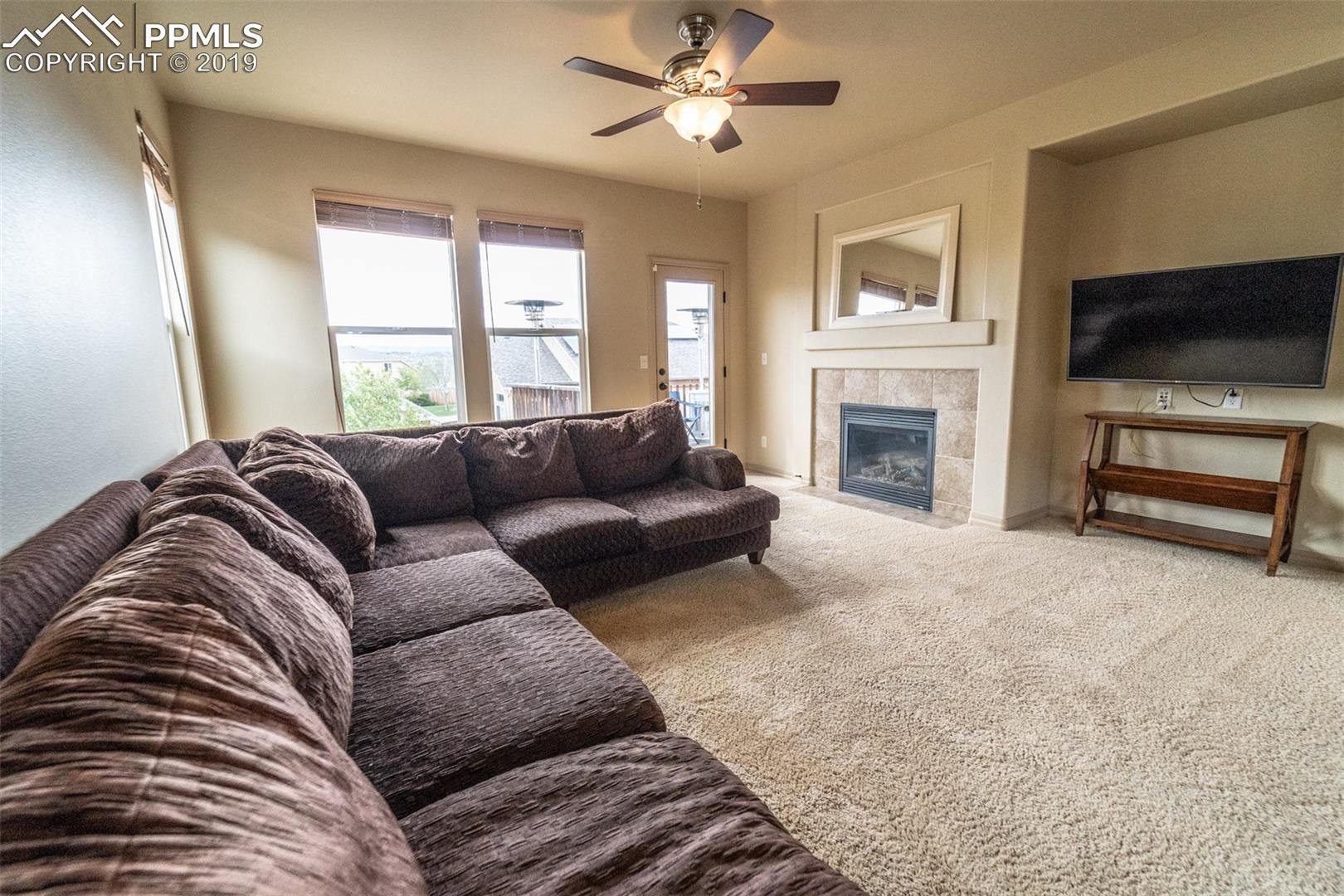 Bright living room with brown sectional sofa, fireplace, ceiling fan, and TV on wall
