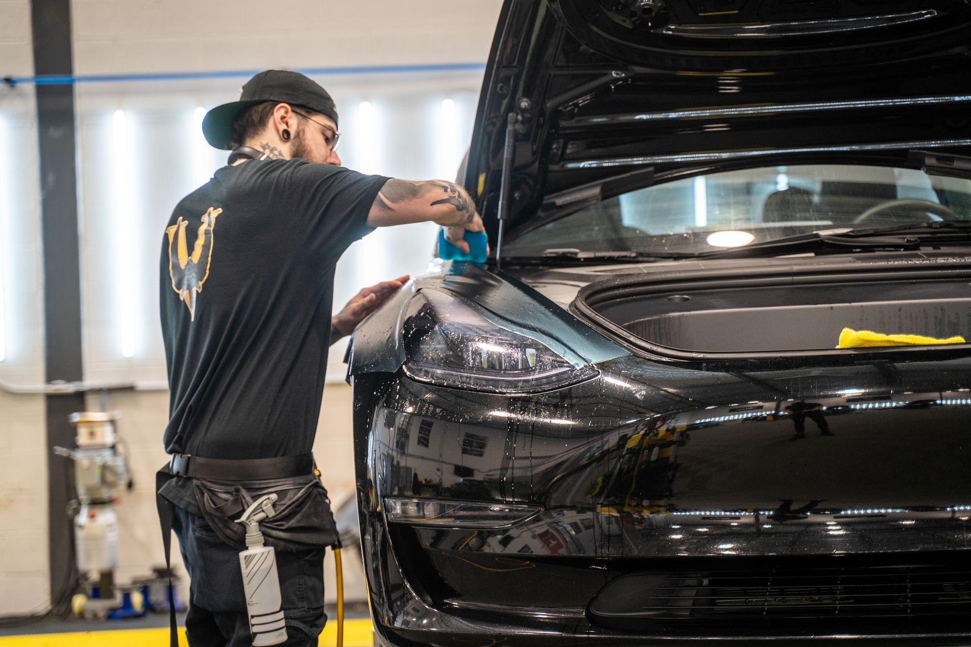A man is polishing the front of a black car in a garage.