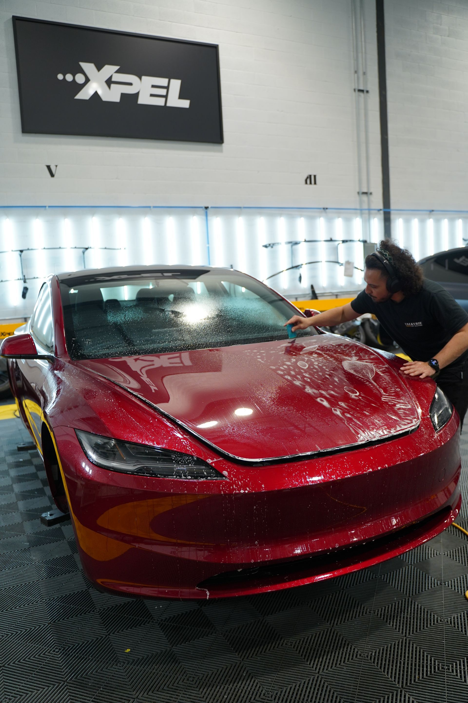 A man is cleaning a red tesla model 3 in a garage.