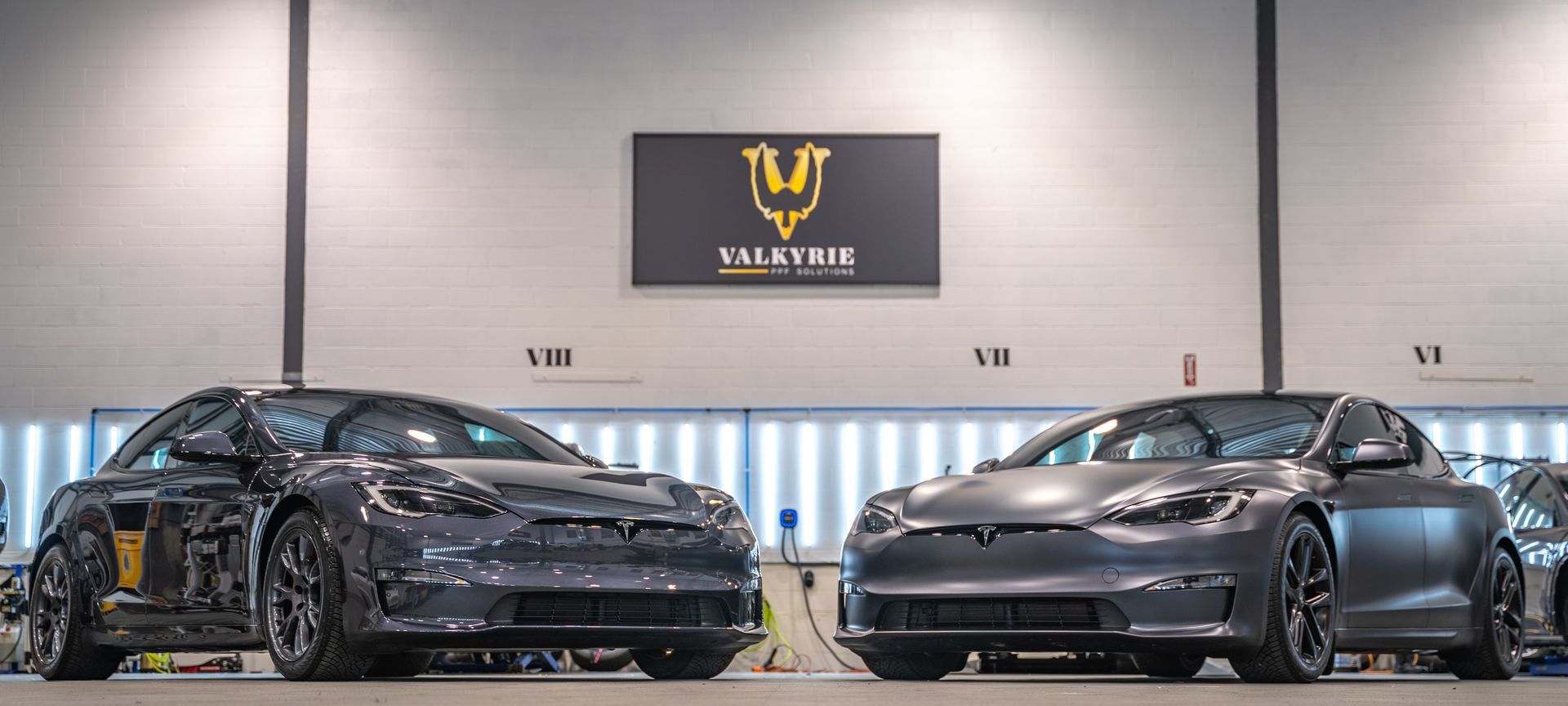 Two tesla model s cars are parked next to each other in a garage.