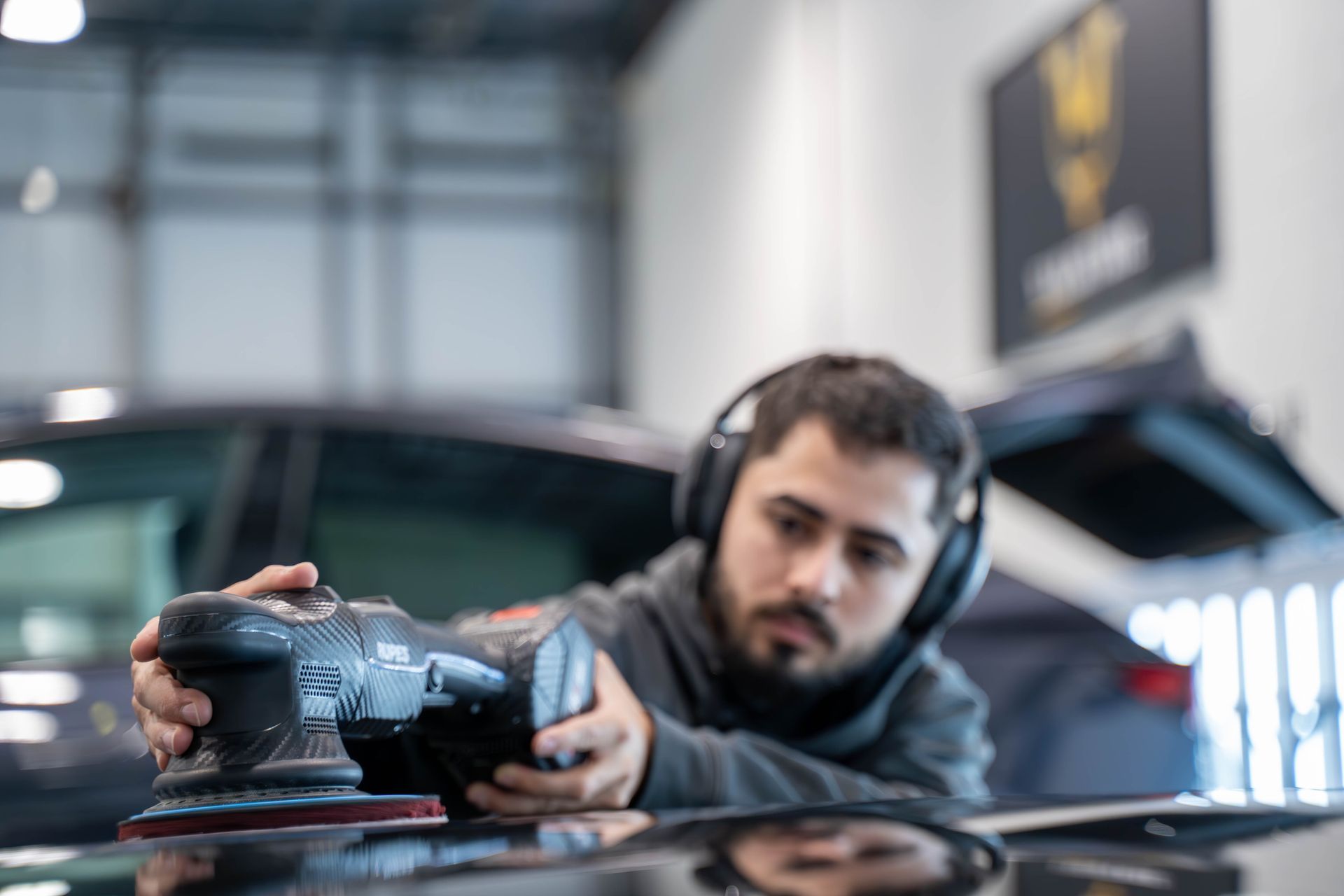 A man wearing headphones is working on the windshield of a car.