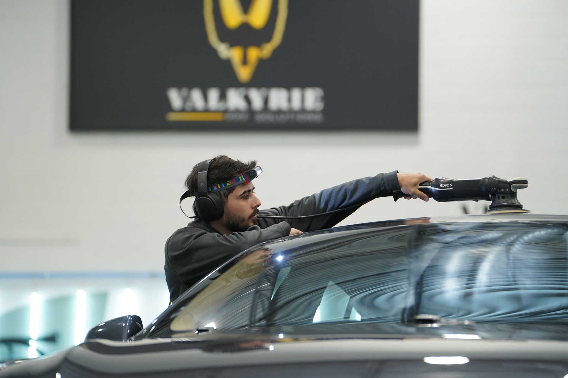 A man wearing headphones is working on the windshield of a car.