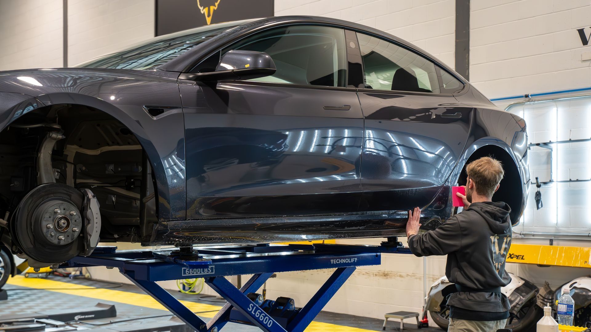 A man is working on a tesla model 3 on a lift in a garage.