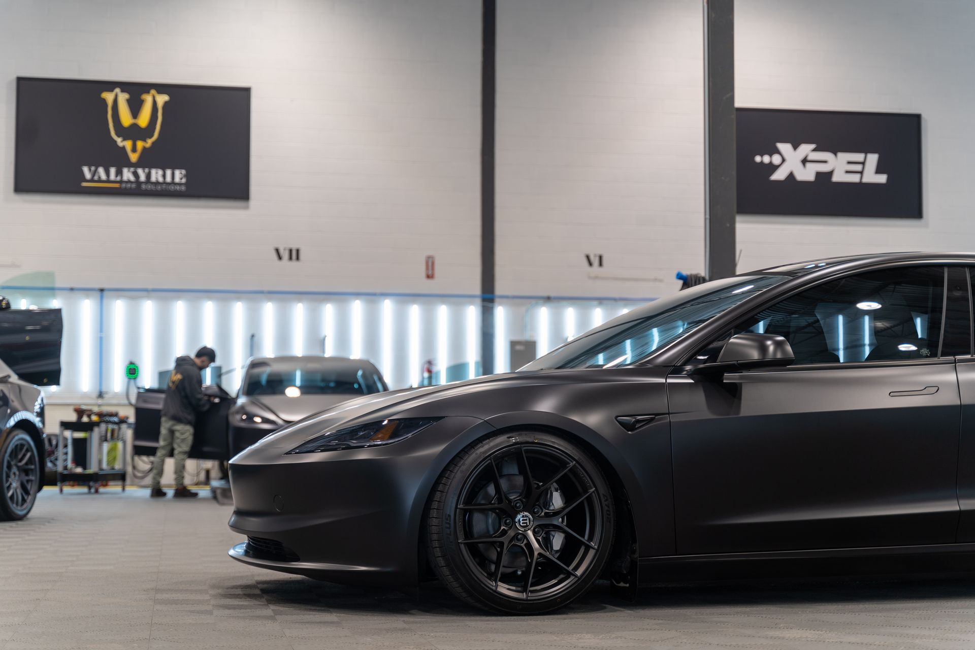 A blue tesla model 3 is parked in a garage.