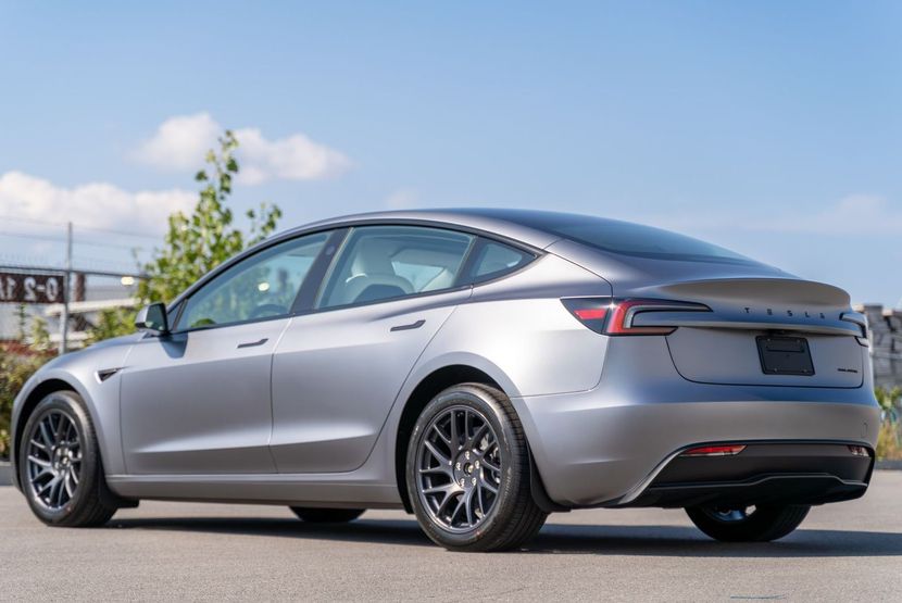 A green tesla model 3 is parked in a garage.