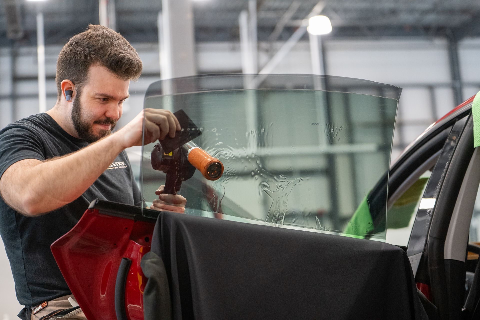 A man is applying tinted glass to a car window in a garage.