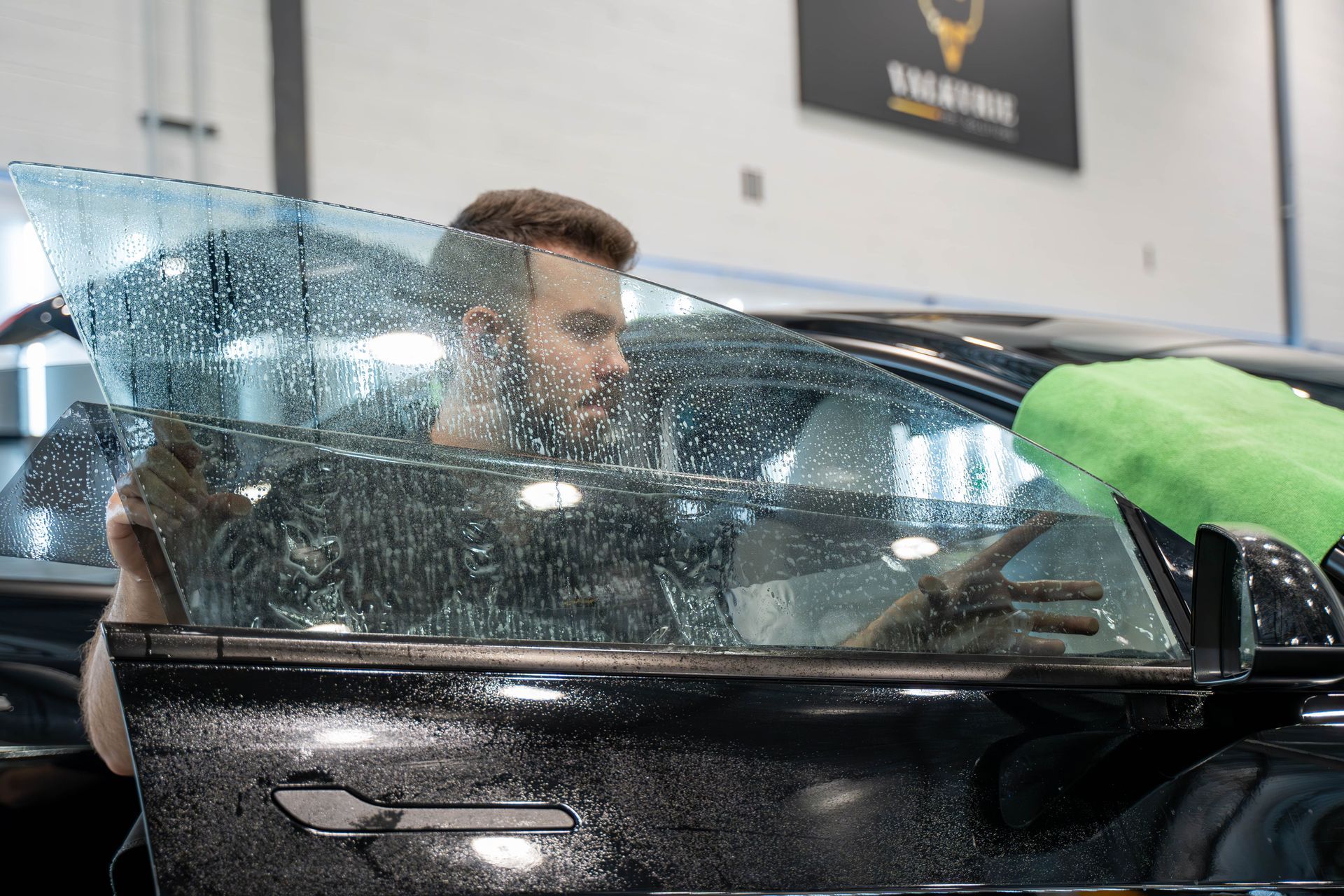 A man is applying tinted glass to a car window in a garage.