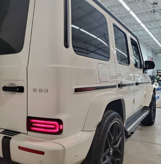 White Mercedes G63 SUV in a garage, rear-left view with pink taillight glowing.
