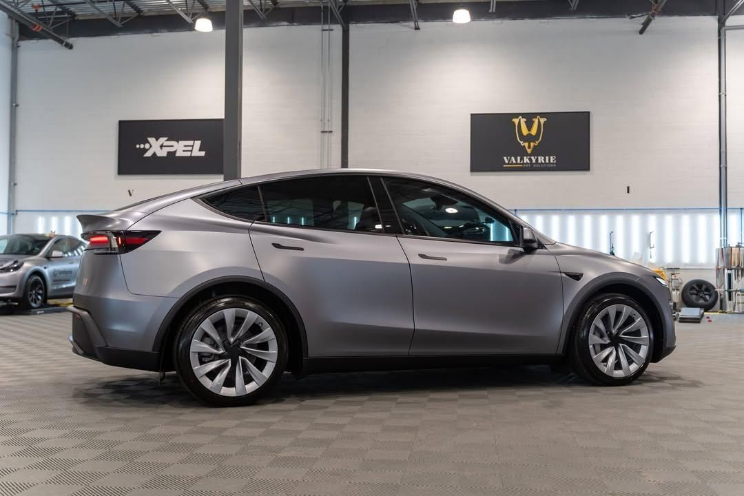 Gray Tesla sedan in a showroom, side view on a tiled floor