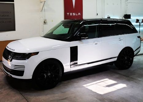 White SUV with black roof and wheels parked indoors under a Tesla sign