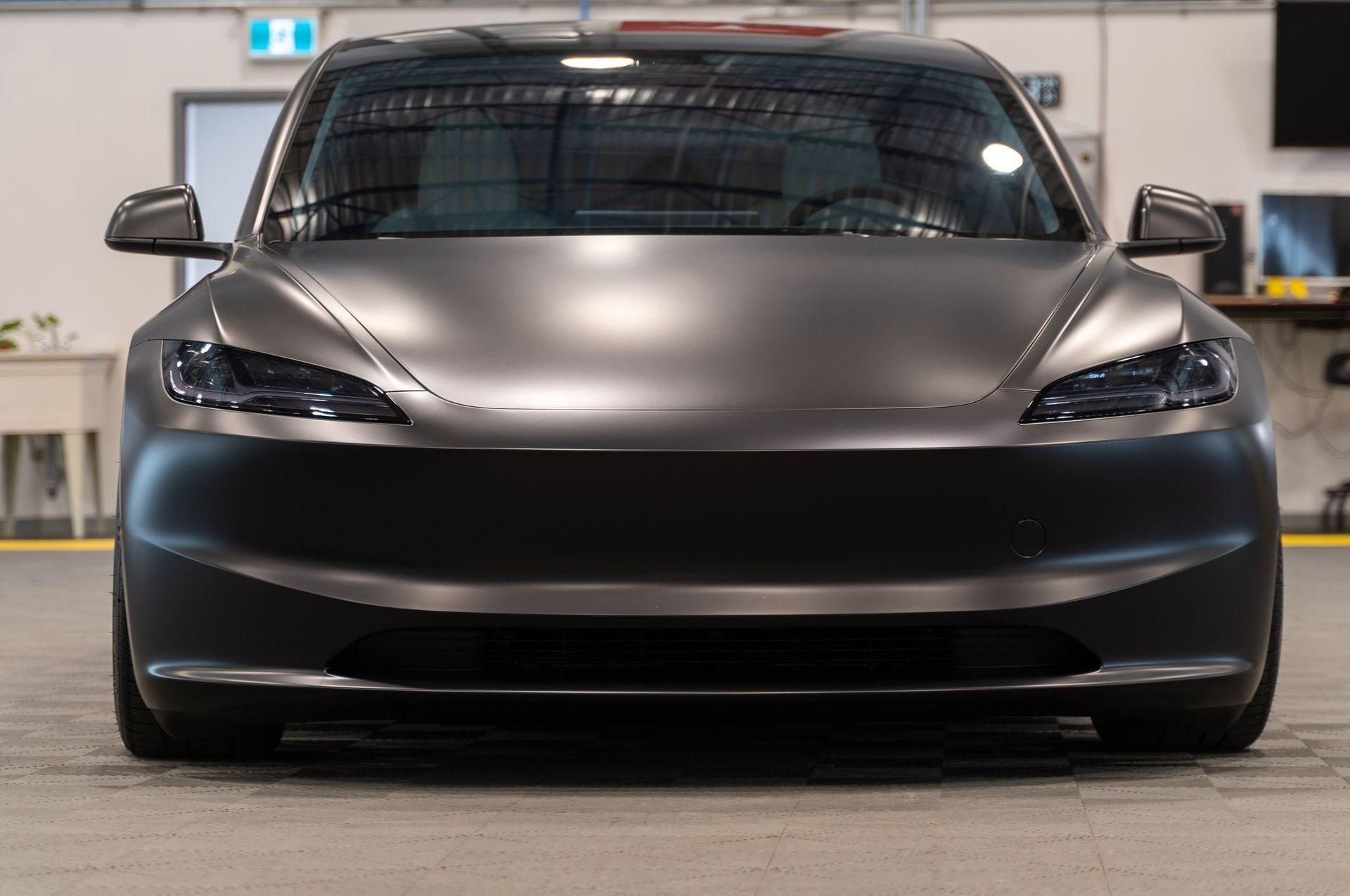 Front view of a matte black Tesla sedan parked indoors in a garage.