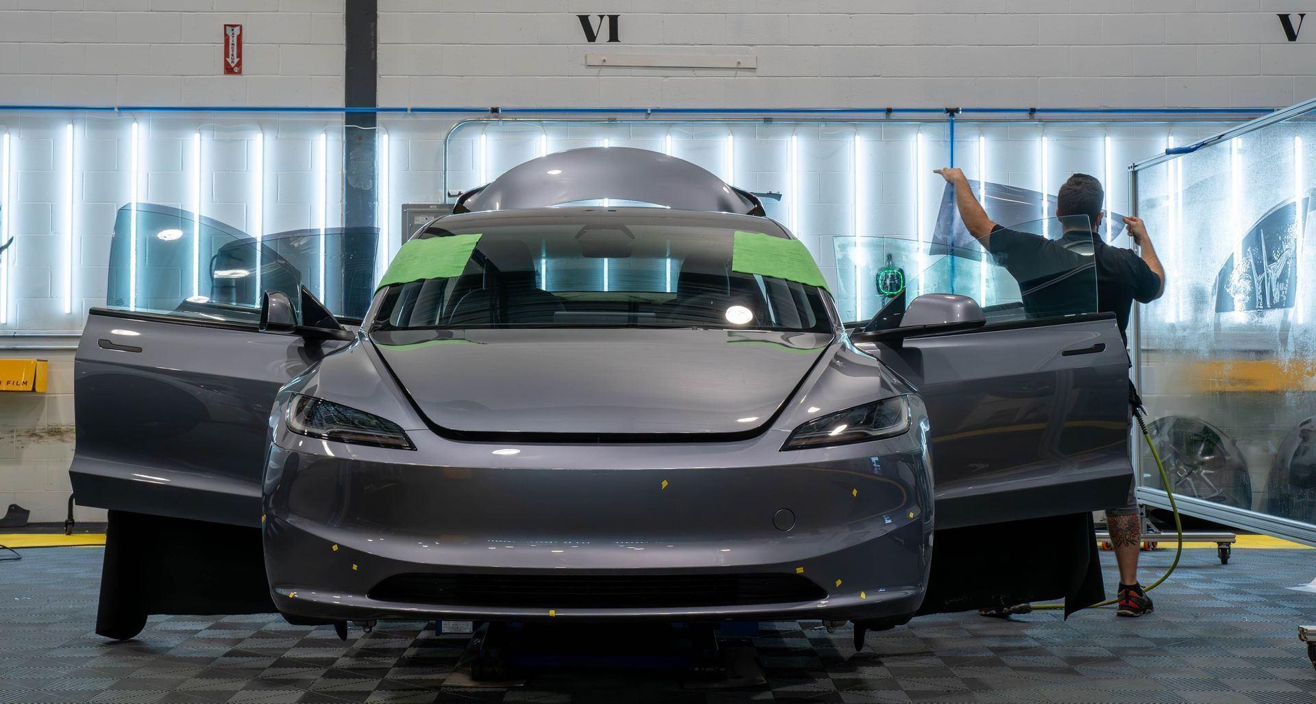 Gray sports car in a test facility with both doors open and a roof-mounted sensor rig