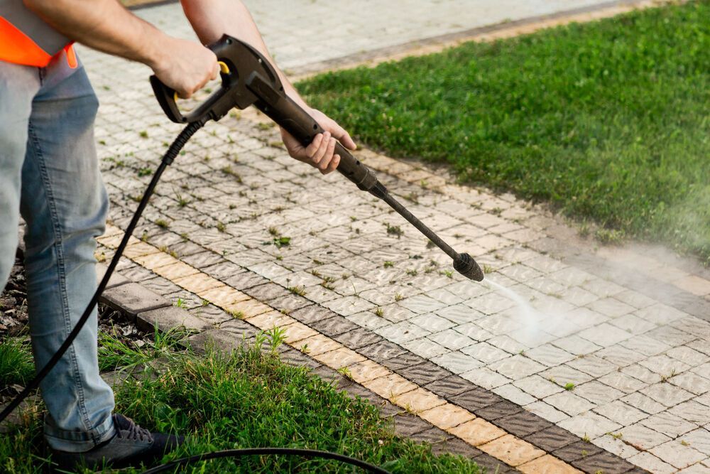 A Man is Using a High Pressure Washer to Clean a Sidewalk — Magic Wand Roof Restoration & Painting in Mermaid Beach, QLD