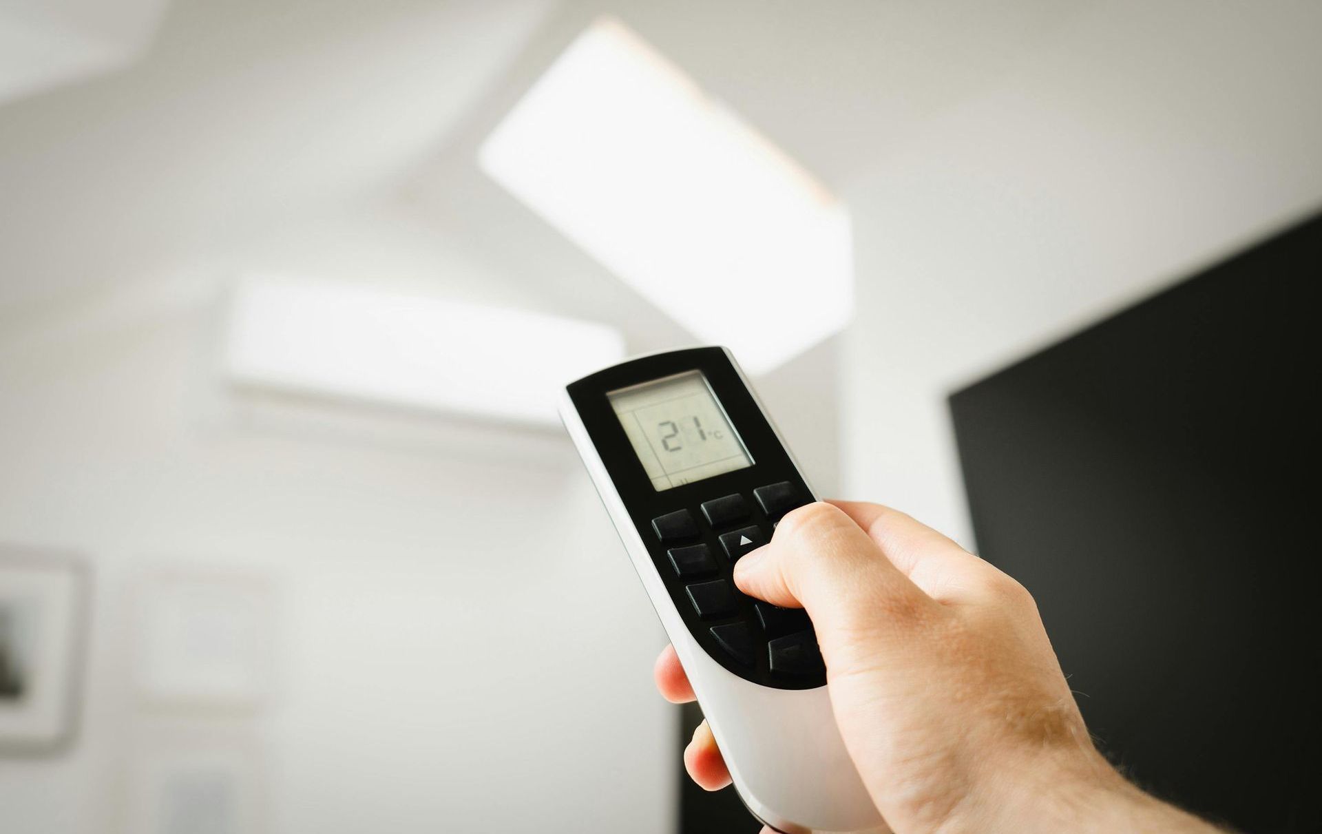 Hand holding an AC remote, adjusting the temperature in a room.