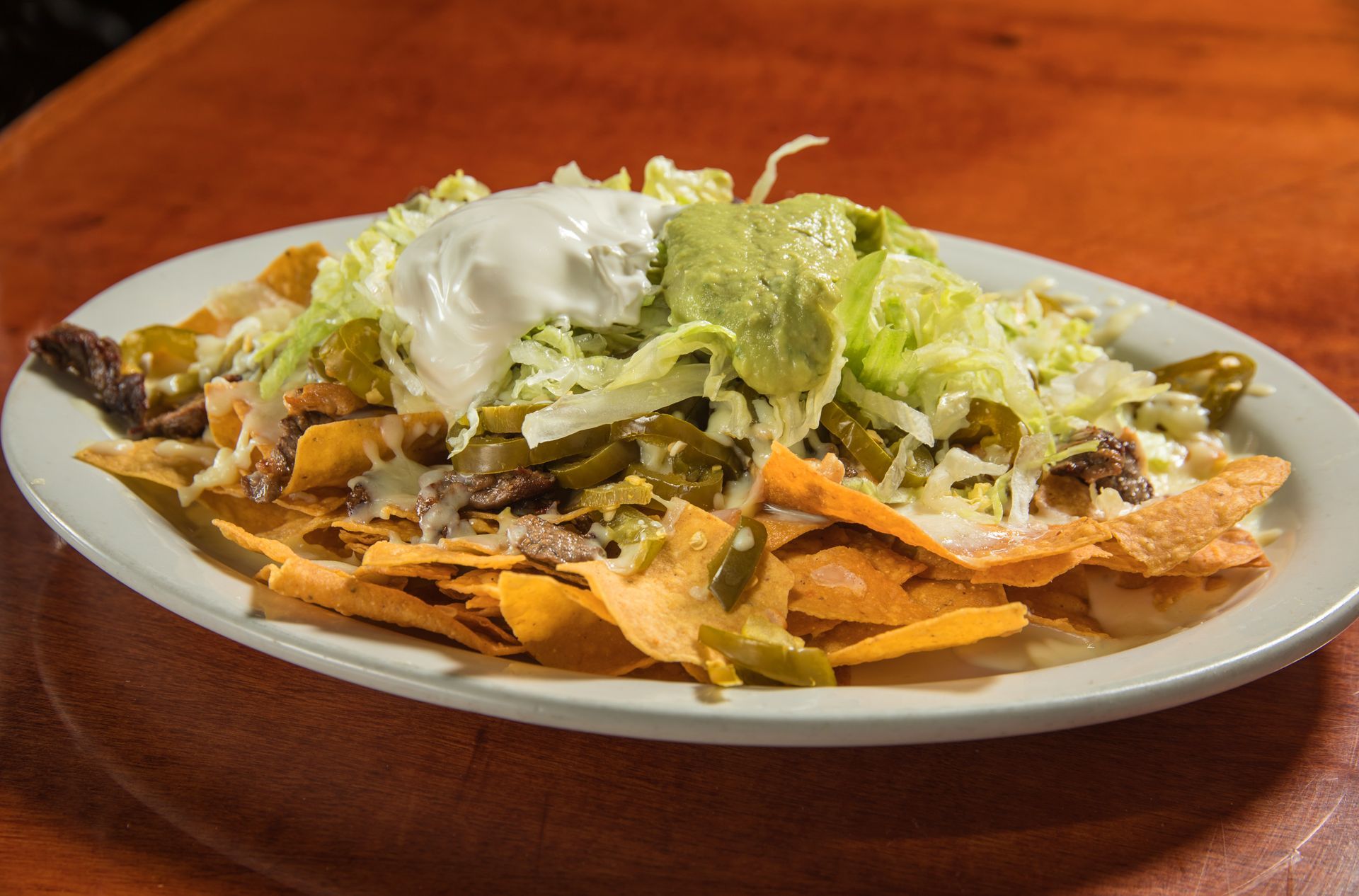 A plate of nachos with lettuce and sour cream on a wooden table.