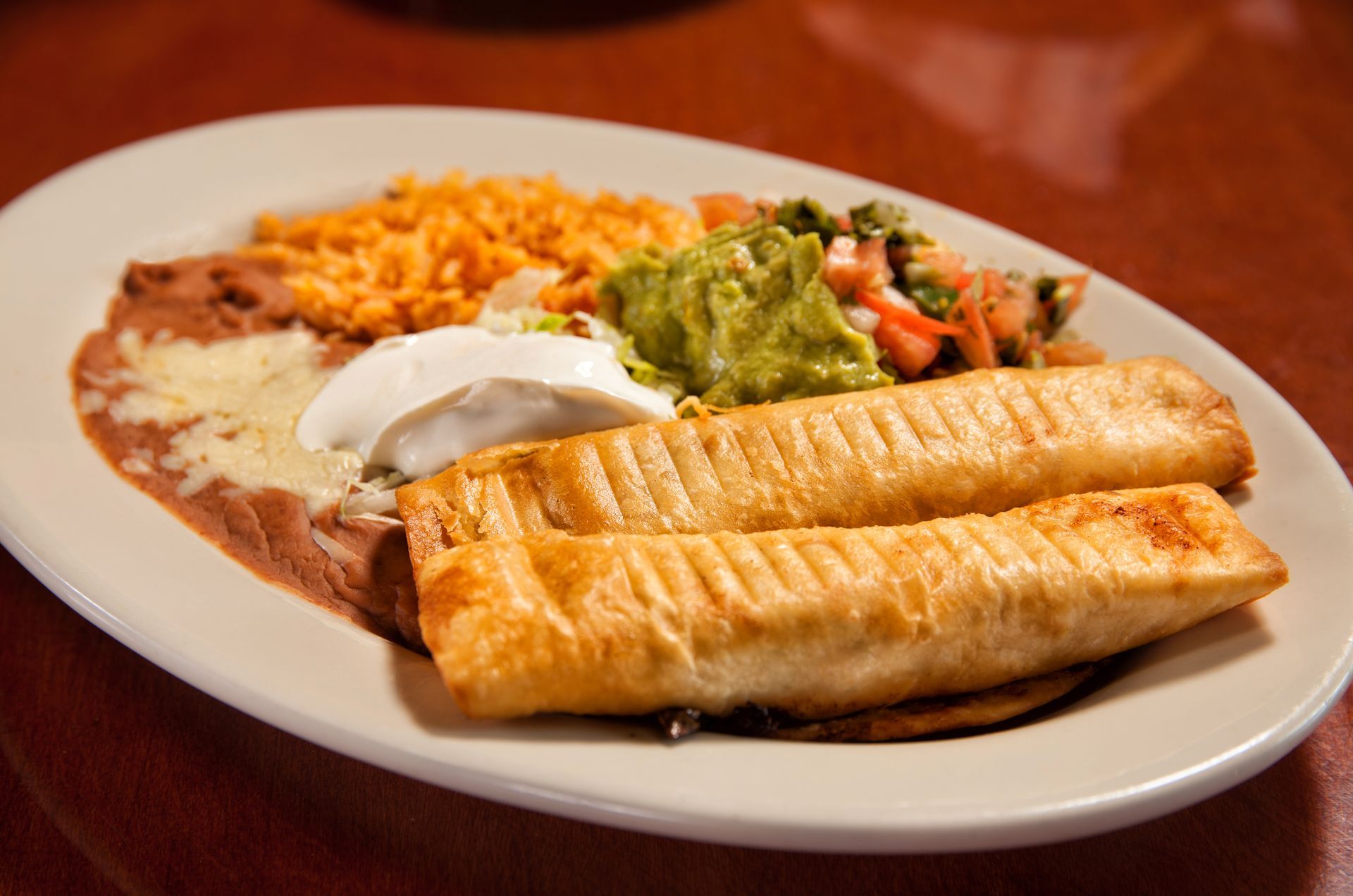 A white plate topped with two tacos , guacamole , rice and beans.