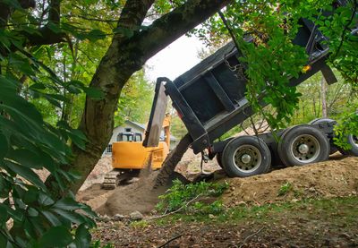 Dump truck unloading dirt into a yellow excavator on a wooded hillside