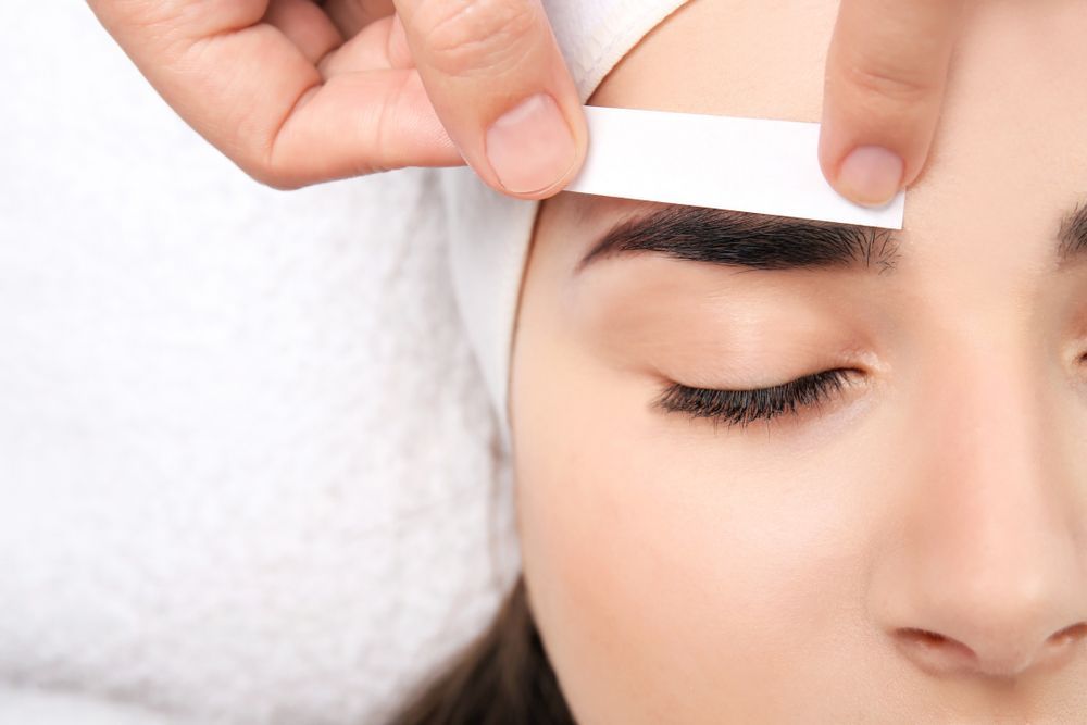 A Woman Is Getting Her Eyebrows Waxed In A Beauty Salon — Mackay Skin Clinic In North Mackay, QLD