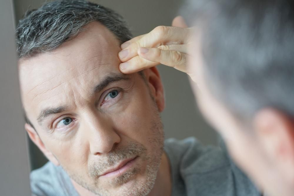 A Man Is Looking At His Face In The Mirror — Mackay Skin Clinic In North Mackay, QLD
