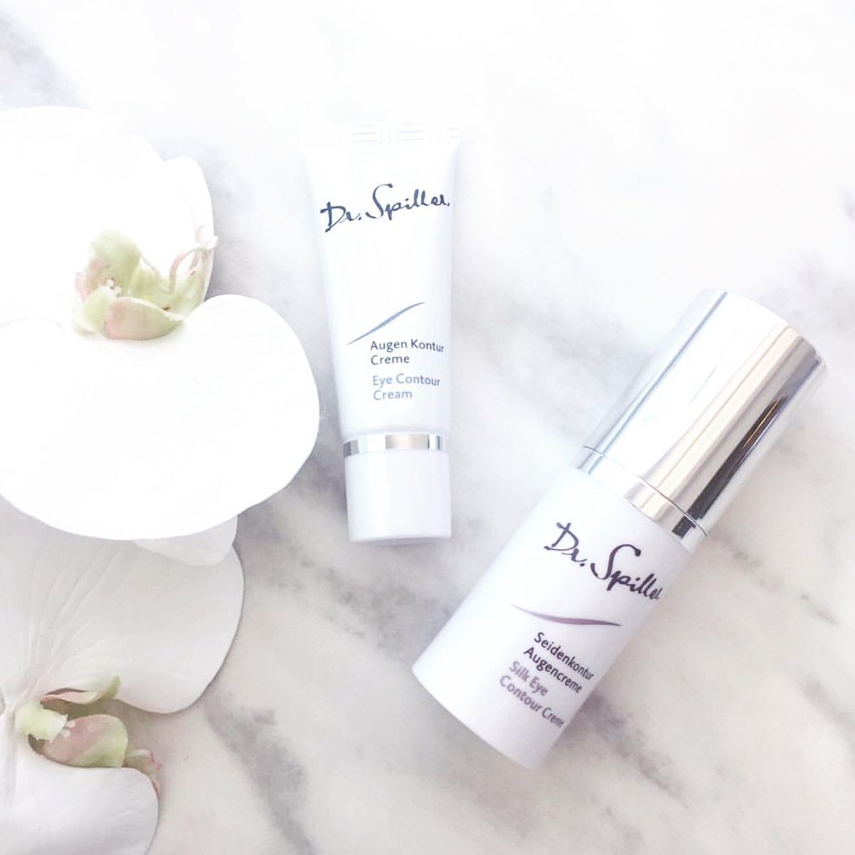 White Dr. Spiller Skincare Tubes on A Marble Surface Beside White Flowers — Mackay Skin Clinic In North Mackay, QLD
