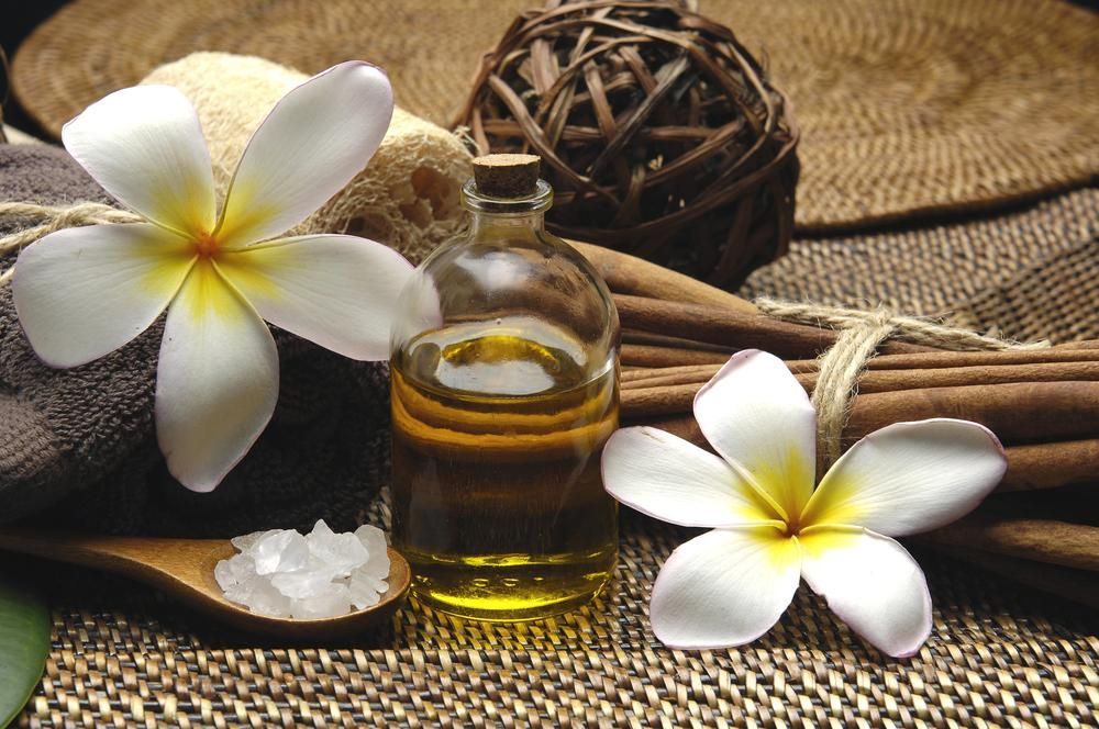 A Bottle Of Essential Oil Sits On A Table Next To Flowers — Mackay Skin Clinic In Bowen, QLD