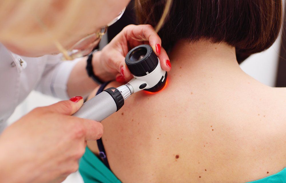 A Doctor Is Examining A Woman's Back With A Magnifying Glass — Mackay Skin Clinic In North Mackay, QLD