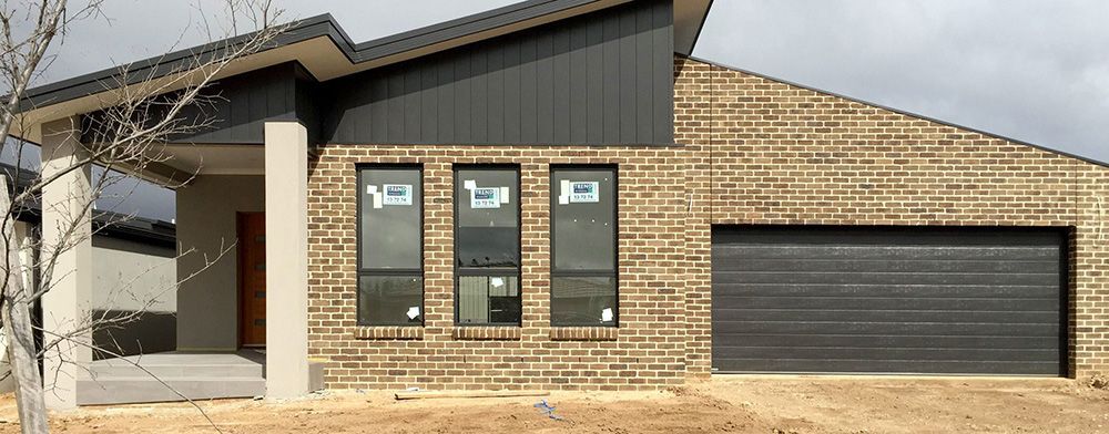 A Brick House With a Black Garage Door and Three Windows — Imperial Build Co. in Coombs, ACT