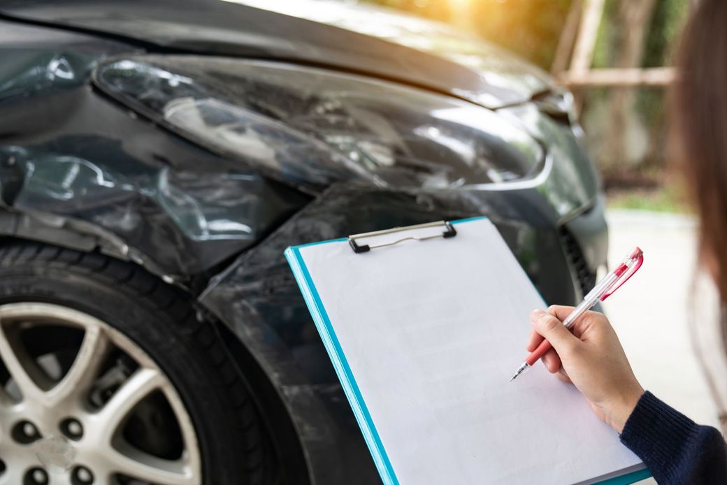 Una donna sta scrivendo su un blocco per appunti davanti a un'auto danneggiata.