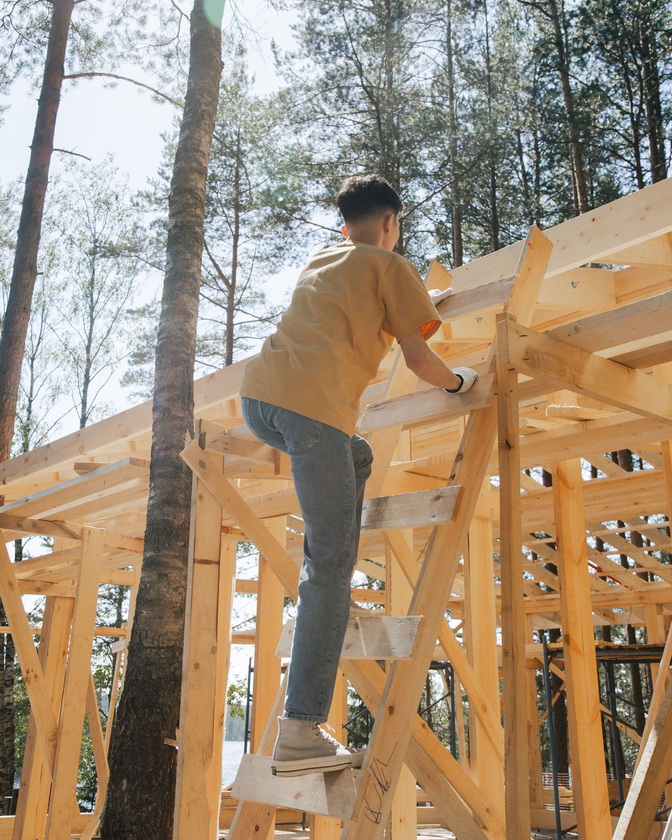 Worker standing on a wooden roof frame at a construction site among tall trees