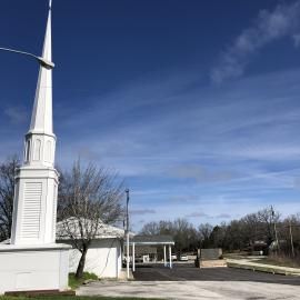 White church steeple against a blue sky beside a quiet road and leafless trees