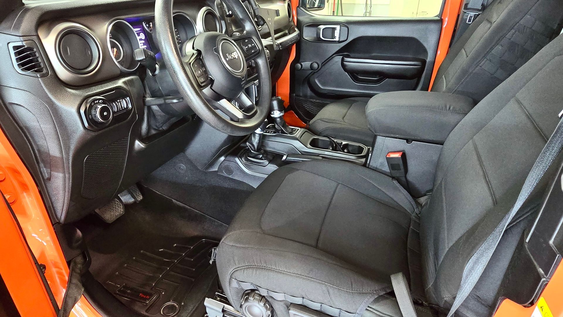 Interior of an orange Jeep, with black seats, steering wheel, and dashboard.