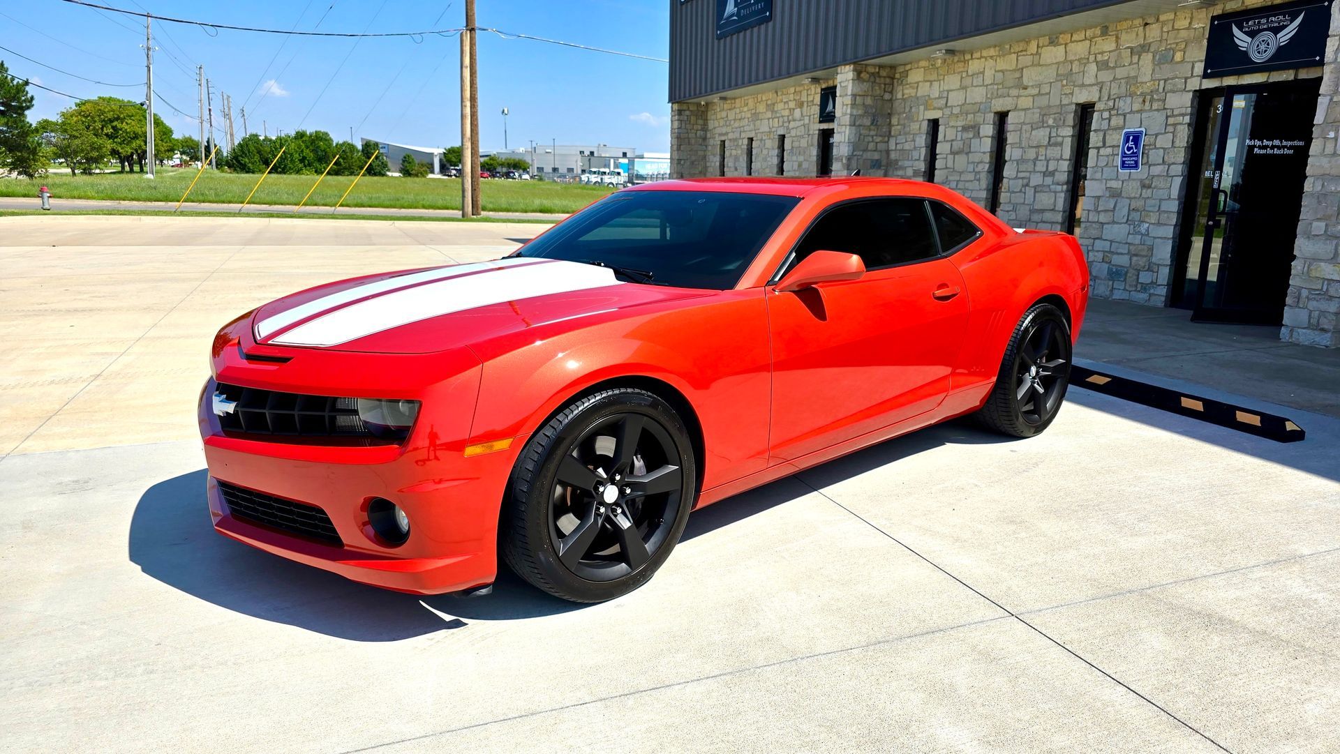 Red Camaro sports car with white stripes, parked in front of a building.