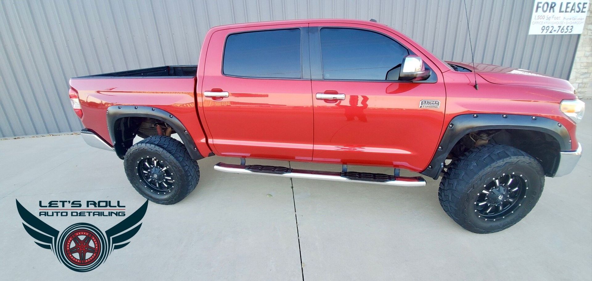 A red truck is parked on the side of the road in front of a building.