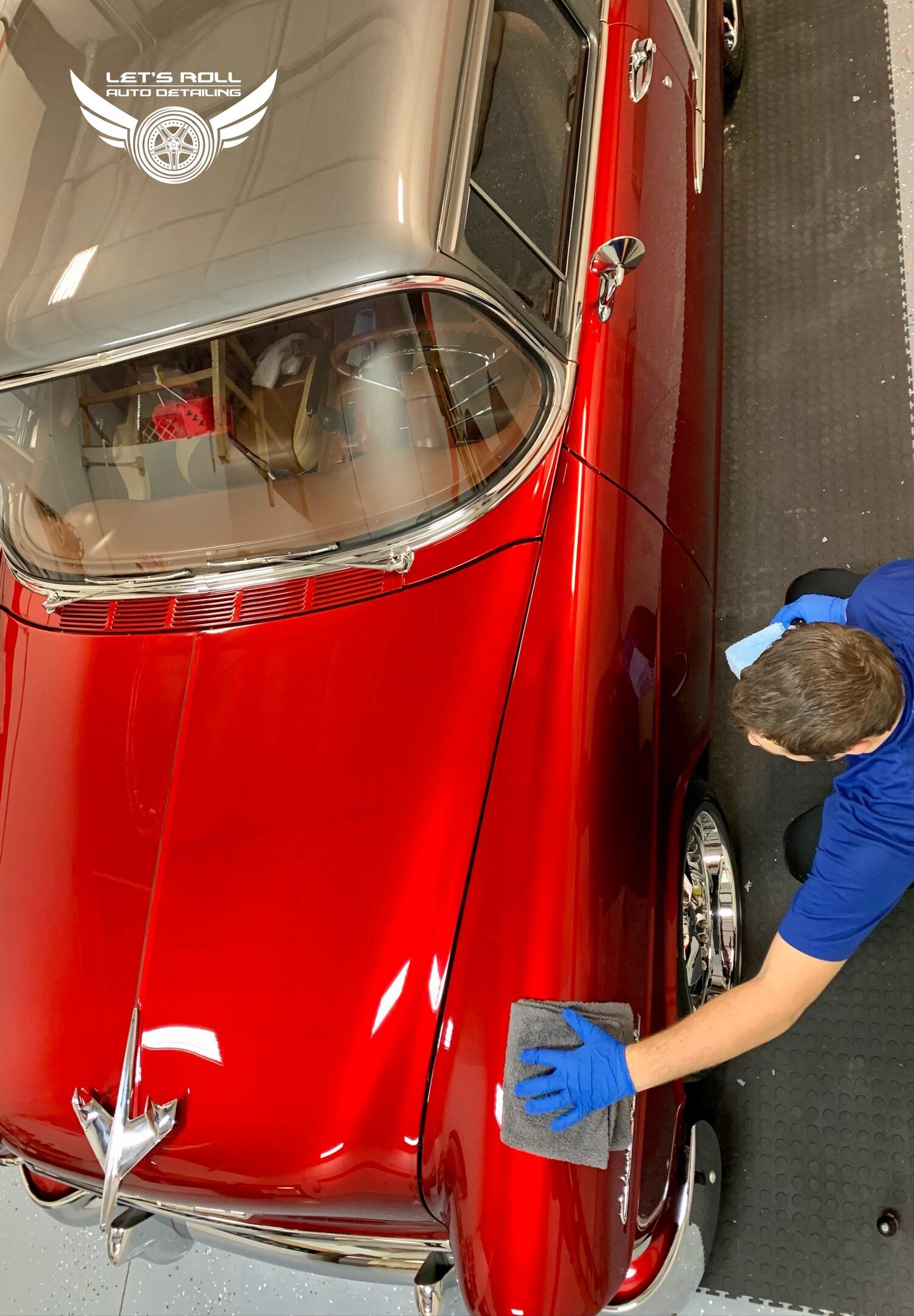 Man in blue shirt polishing a shiny, red vintage car with a chrome bumper.