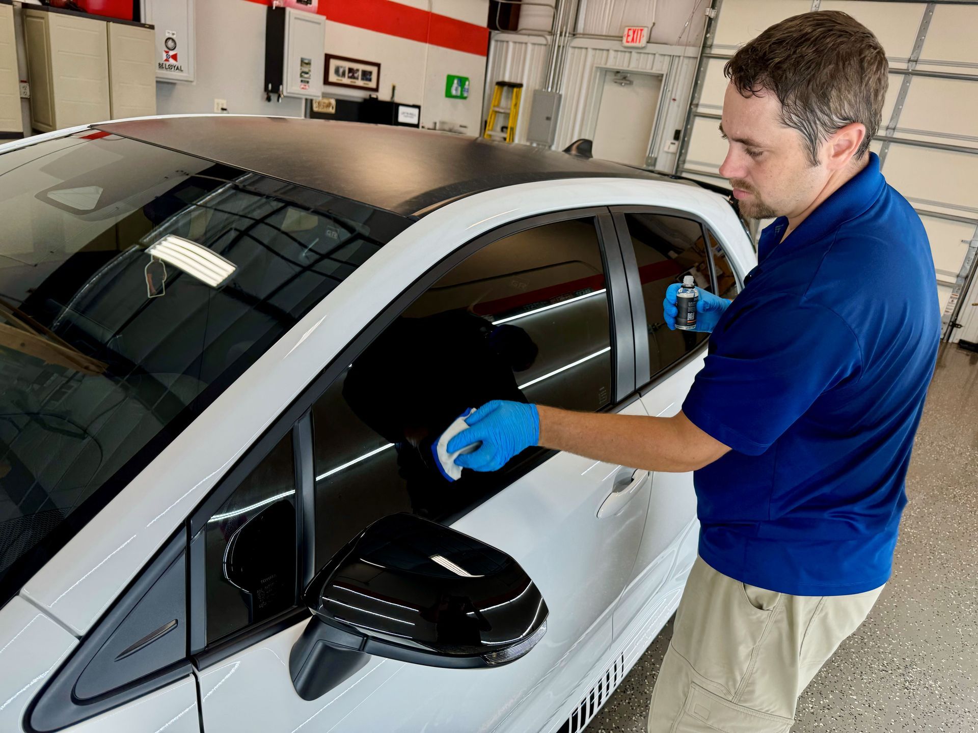 A man in a blue shirt is cleaning the windows of a white car.