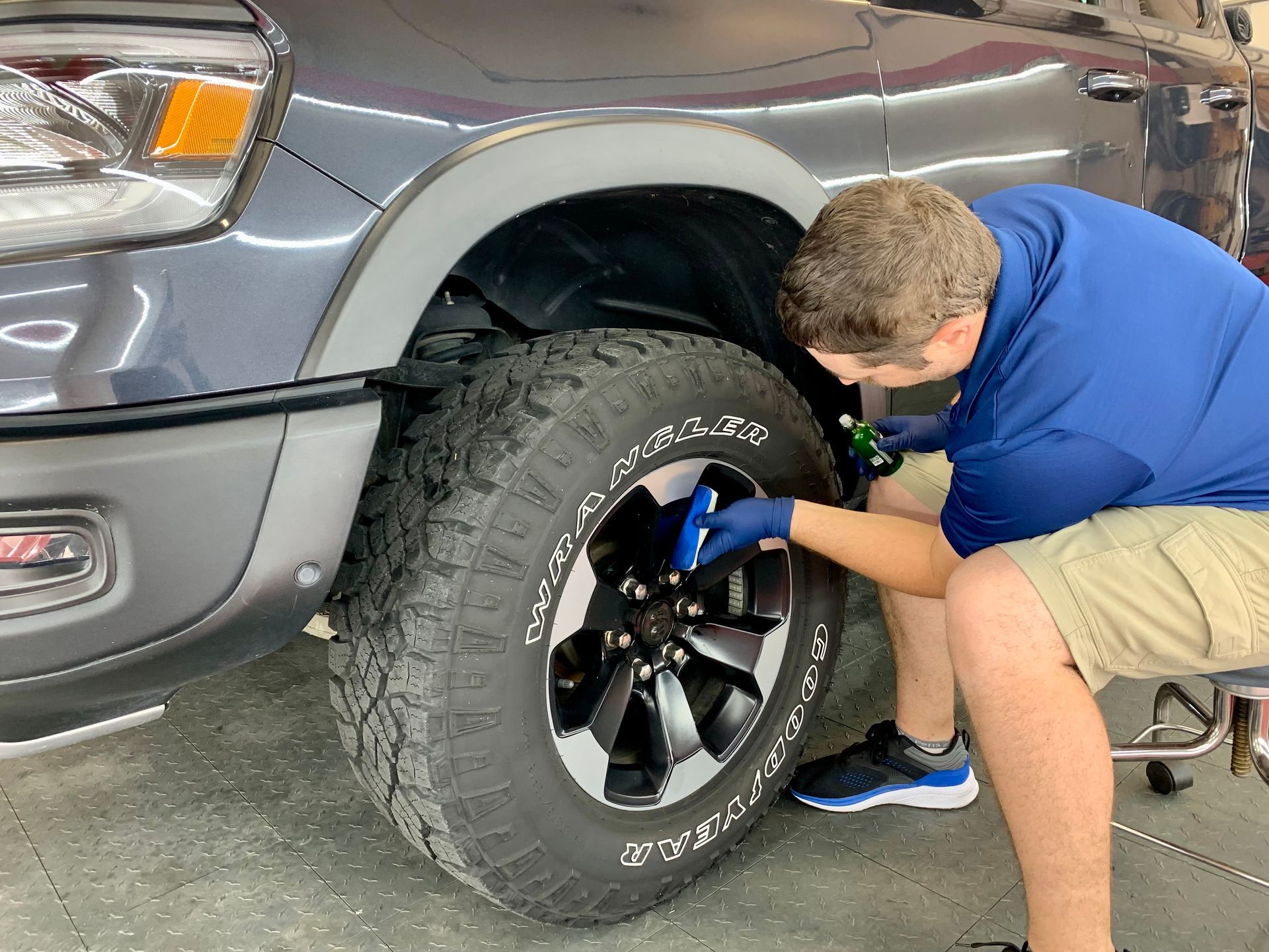 Man working on the front tire of a gray truck, using a tool.