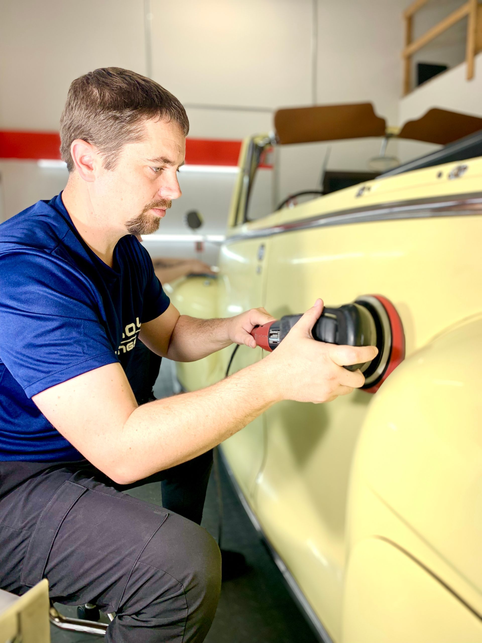 Man polishing a yellow car with a power tool in a garage.