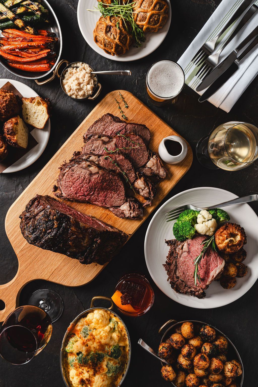Roast beef with carrots, bread, vegetables, a pint of beer and glass of wine.