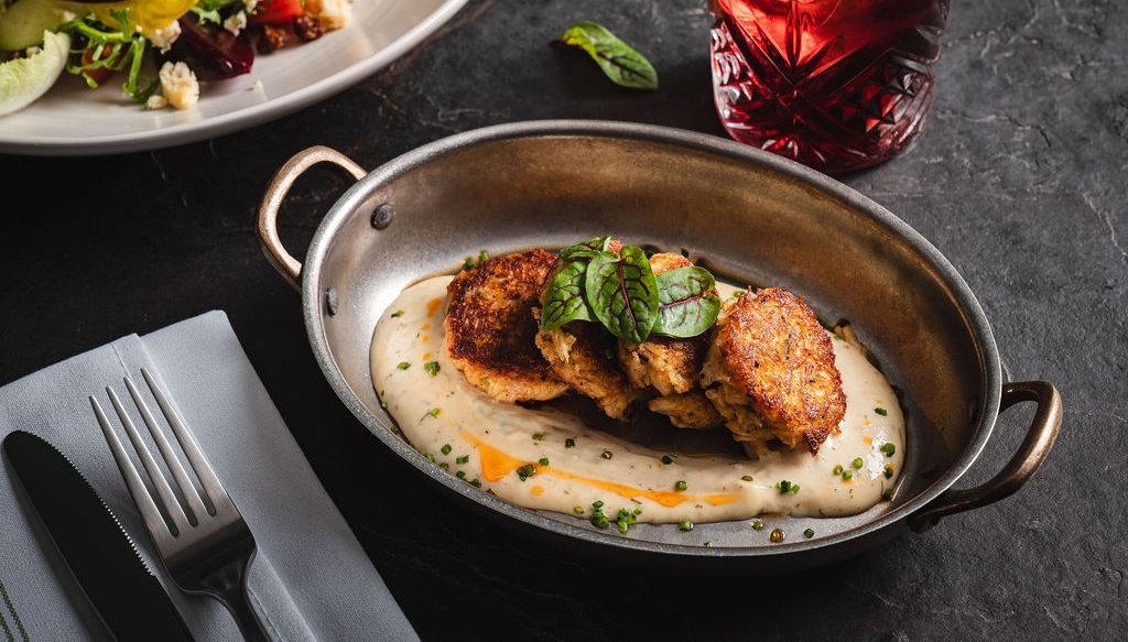 Carb cakes in creamy sauce in a skillet, with salad and a red drink on a dark table