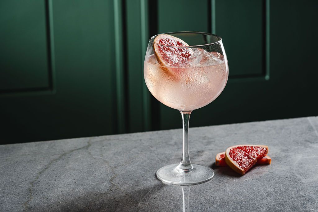 Pink cocktail in a stemmed glass with a grapefruit garnish on a gray table