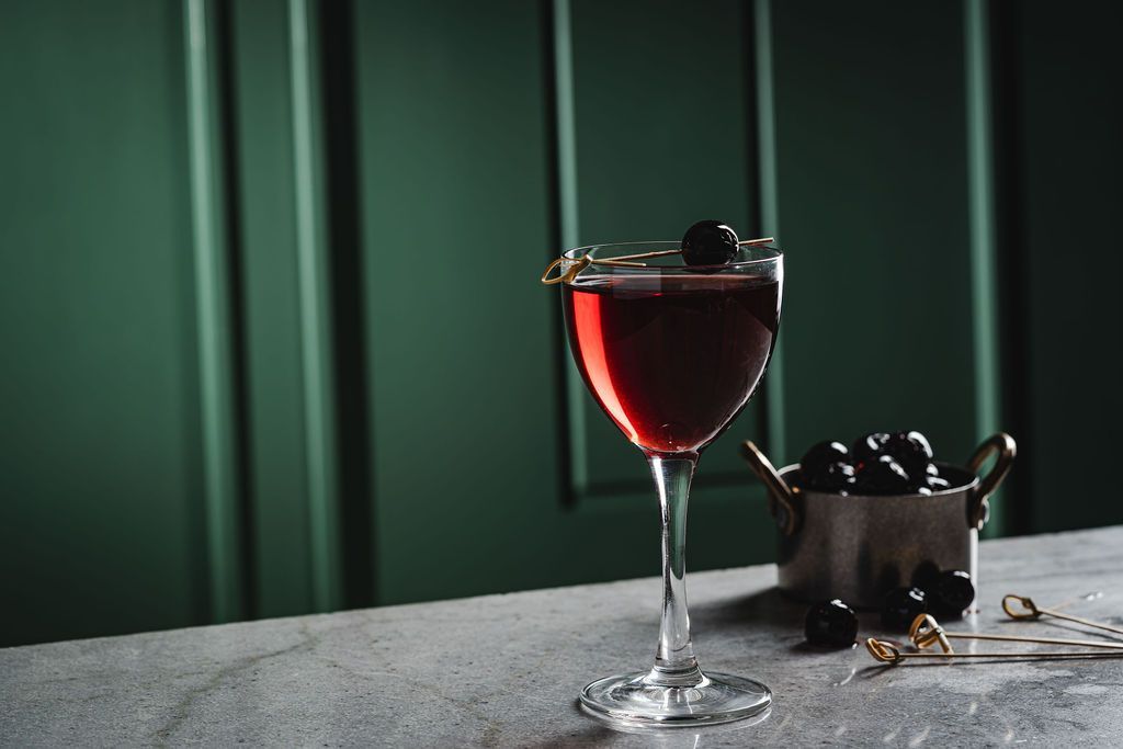 Red cocktail in a stemmed glass on a gray table.