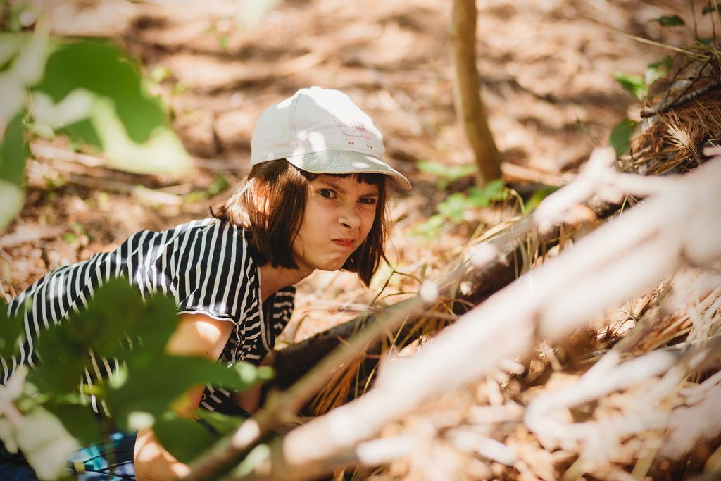A young girl wearing a white hat is kneeling down in the woods.