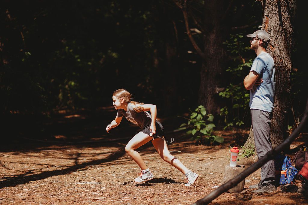 A man is watching a girl run in the woods.