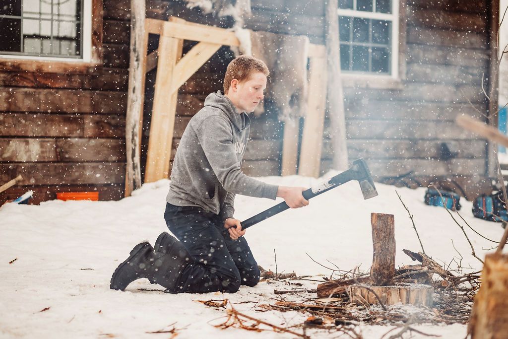 A teenage boy is learning survival training by chopping wood for a campfire