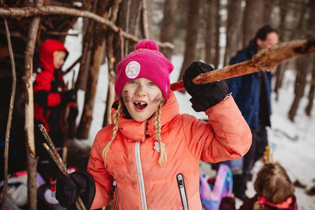 A little girl in a pink hat is holding a stick in the snow.