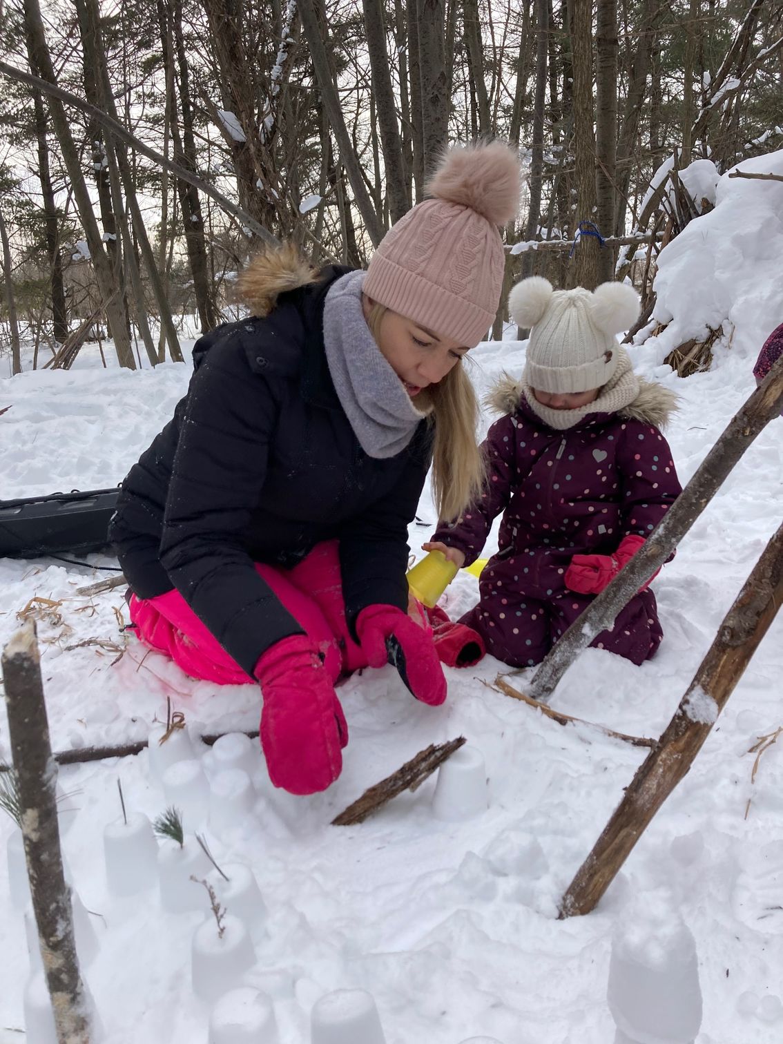 A woman and a child are playing in the snow during forest preschool