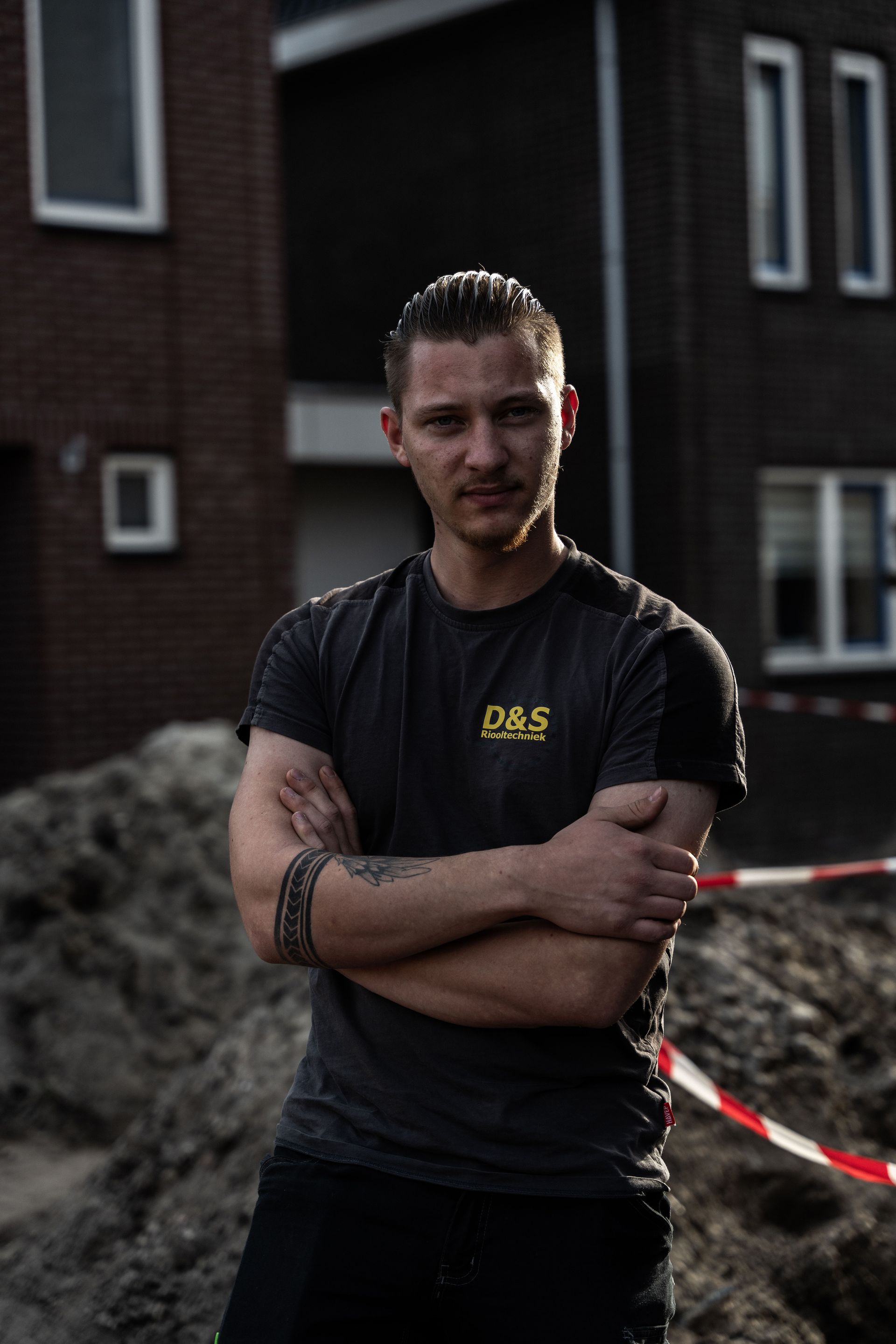 Een man staat met zijn armen over elkaar voor een gebouw.