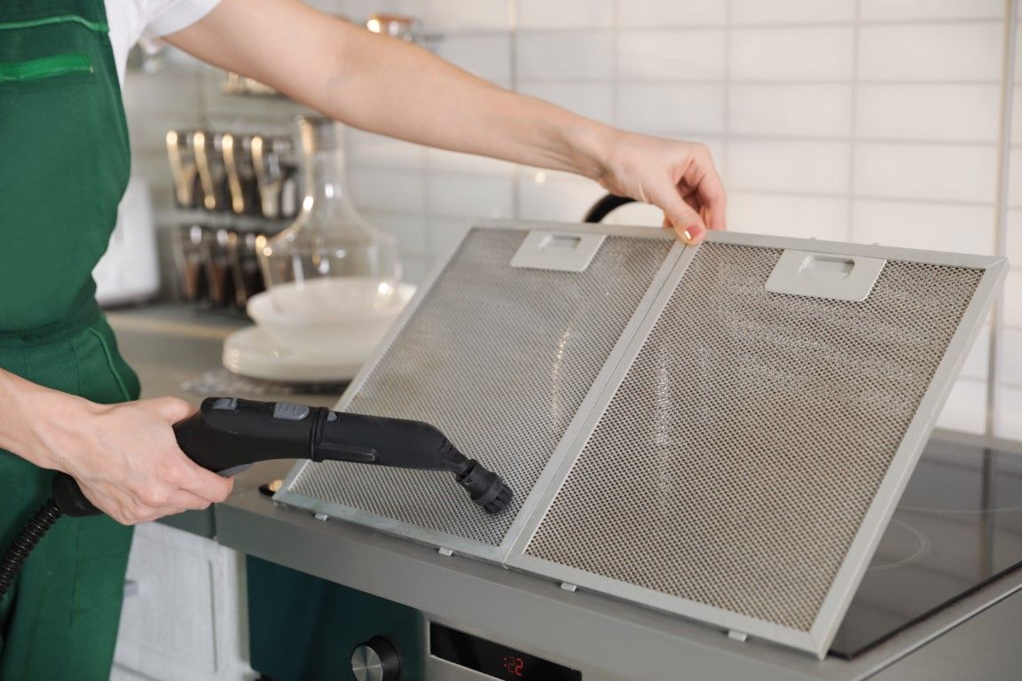 Person cleaning a metal kitchen range hood filter with a vacuum cleaner