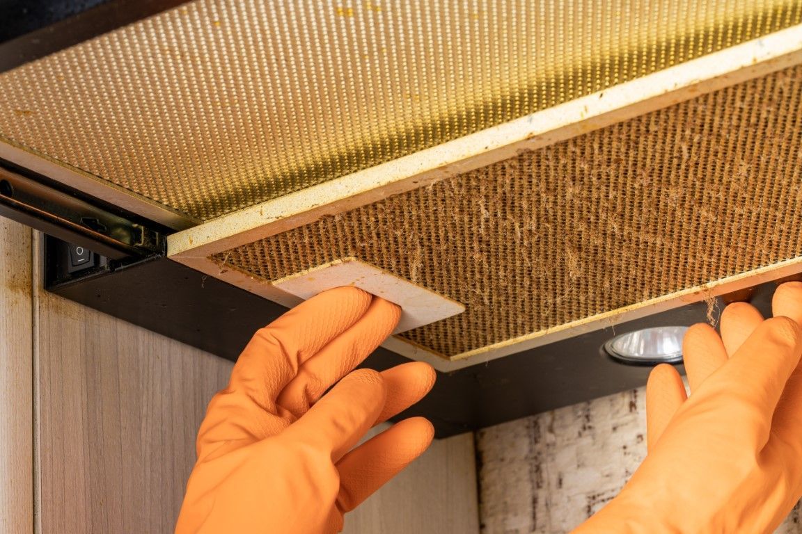 Gloved hands removing a vent filter from beneath a cabinet