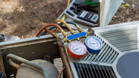 An air conditioner being serviced with gauges and hoses connected outside.